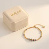 Pulsera elástica de cuentas doradas con baño de oro, intercaladas con dijes de ojos turcos en tonos azul, blanco y negro.