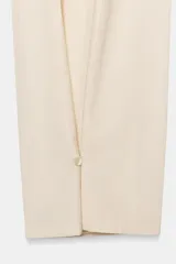 Pantalón de tiro medio color beige claro, de corte ancho y fluido, con pliegues marcados en el delantero y cintura ajustable con cordones. Presenta un detalle de pliegue con botón en el bajo.