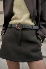 Falda pantalón corta de tiro medio color beige claro, con cierre frontal y detalle de cinturón negro con hebilla metálica redonda dorada.