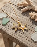 Collar de bronce con cadena fina y doble dije colgante en forma de estrella de mar, uno de ellos pavimentado con circonias y el otro con una perla central.