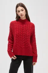 Polera de tejido de punto color crema, con cuello alto y diseño de trenzas verticales. Presenta mangas largas con puños acanalados y un corte holgado.