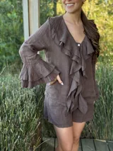 Camisa de lino azul marino con volados en cascada a lo largo del frente y en los puños de las mangas largas. Presenta un escote en V con un botón de nácar visible.