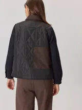 Campera de diseño híbrido con frente acolchado en color tostado, solapas y cuello en tejido de lana con patrón de cuadros tipo príncipe de gales, y mangas en paño de lana color azul marino. Cuenta con cierre frontal de botones.