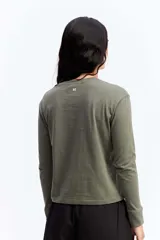 Remera de manga larga color verde oliva, con cuello redondo y estampa gráfica pequeña en el pecho con texto y dibujos lineales.