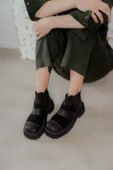Botas de caña baja con punta cuadrada, confeccionadas en una combinación de cuero liso y gamuza en tonos marrones. Presentan un diseño con múltiples cortes y costuras visibles, cierre elástico lateral y suela de goma dentada tipo track.