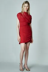 Vestido corto de color rojo confeccionado en tejido mesh. Presenta cuello subido, diseño sin mangas con frunces en los hombros y falda con drapeado lateral. Incluye cierre lateral con cremallera oculta.