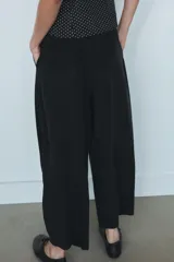 Pantalón fluido de tiro medio color verde militar, con cintura elástica en la parte trasera, pinzas en el delantero y bolsillos laterales ocultos en la costura. Presenta un diseño de pernera ancha y corte tobillero, con cierre frontal de cremallera y botón.