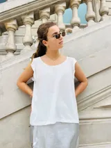 Blusa blanca sin mangas con cuello redondo y detalle de volados en los hombros.