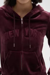 Campera con capucha de terciopelo color bordó, con cierre frontal, bolsillos tipo canguro y texto bordado en el pecho.