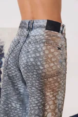 Pantalón de denim tiro medio con silueta amplia y corte recto. Presenta un diseño bicolor con estampado tipo animal print en tonos grisáceos y marrones, con bolsillos laterales y traseros.