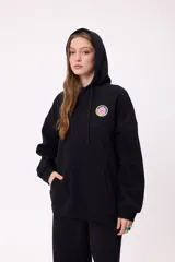 Canguro negro con capucha y bolsillo frontal tipo canguro. Presenta un pequeño estampado circular en el pecho con diseño colorido y logo de la marca.