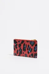 Monedero de tamaño grande con estructura rígida y exterior con textura brillante, estampado animal print en tonos rojo, negro y azul. Cuenta con cierre de cremallera dorado, logo metálico de Bimba y Lola y tarjetero interior.