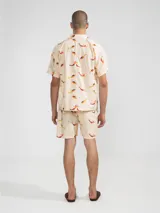 Bermudas de algodón color crema con estampado de sirenas en tonos naranja y marrón. Tiene cintura elástica con cordón ajustable, dos bolsillos laterales y un bolsillo trasero.