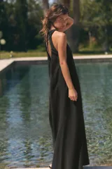 Vestido midi de corte fluido y diseño minimalista, con cuello redondo y mangas sisa. Presenta un cierre en la espalda con abertura y lazada ajustable.