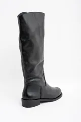 Bota de caña alta confeccionada en cuero legítimo negro, con diseño de textura granulada en la parte superior y acabado liso en la puntera. Cuenta con un taco bajo y suela plana.