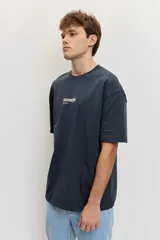 Remera de corte oversize color blanco tiza, de manga corta y cuello redondo, con pequeño estampado gráfico azul en el pecho.