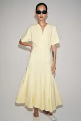 Vestido largo de Zara Woman Collection color amarillo claro, confeccionado en mezcla de algodón. Cuenta con escote en V, manga corta, corte en la cintura y falda evasé con pliegues marcados.