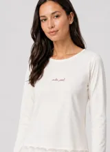 Pijama de algodón color crema, compuesto por una remera de manga larga con cuello redondo y detalle de texto bordado en el pecho, y terminación con puntilla en el ruedo.