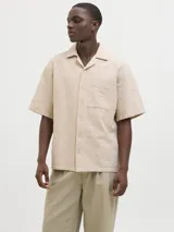 Camisa de manga corta color beige con cuello resort y cierre de botones. Confeccionada en tejido jacquard con mezcla de algodón y lino.