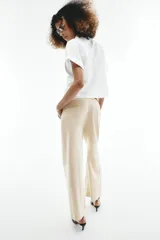 Pantalón culotte de tiro alto color beige, confeccionado con lino. Presenta pernera ancha y corta, bolsillos delanteros y falsos bolsillos de vivo en la espalda. Incluye un cinturón marrón con hebilla metálica redonda y cierre frontal con cremallera, botón interior y gancho.