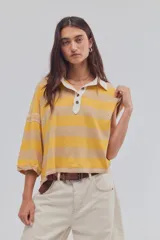 Remera tipo polo de algodón con diseño a rayas horizontales en tonos amarillo y beige, corte oversize, cuello clásico blanco y cierre frontal con botones.