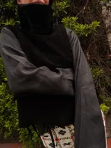 Chaleco negro de gamuza con cuello de pelo sintético y diseño estructurado, con lazos laterales para ajuste.