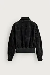 Cazadora cropped fit de piel con acabado serraje y textura de ante, color negro. Presenta cuello camisero, cierre frontal con cremallera, bolsillos delanteros de plastrón con solapa en el pecho y acabado de rib elástico en los puños y el bajo.