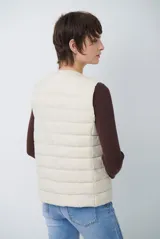 Chaleco acolchado tipo puffer, color beige, sin mangas, con cuello redondo y cierre frontal con botones a presión.
