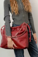 Bolso tipo tote de cuero color rojo con patrón acolchado de rombos y cadena plateada en las asas.