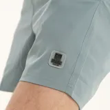 Short de baño liso color verde azulado, con cintura elastizada y cordón de ajuste blanco. Posee un pequeño parche con logo en la parte inferior delantera derecha.