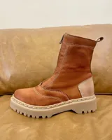 Bota tipo borcego de cuero color marrón oscuro con detalles en gamuza beige en el talón. Presenta cierre frontal, suela track de goma color beige con costuras visibles y forro interior de felpa.