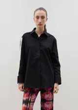 Camisa negra de corte holgado con cuello clásico y cierre frontal de botones. Presenta una franja lateral en color crema a lo largo de las mangas y tajos en los laterales del ruedo.