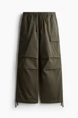 Pantalón cargo verde militar de tejido de algodón, corte holgado con cintura elástica y cordón ajustable. Presenta múltiples bolsillos con solapa en las piernas y cordones de ajuste en los bajos.