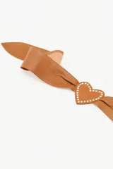 Cinturón faja de cuero ovino color suela, con diseño de hebilla en forma de corazón y detalle de tachas metálicas en todo el contorno.