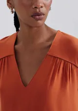 Blusa naranja sin mangas con escote en V y detalle de frunces en los hombros.