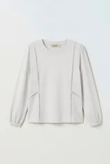 Remera manga larga de color beige, con cuello redondo y detalles de encaje calado en la parte frontal. Cuenta con mangas abullonadas y puños elásticos.