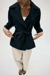 Chaqueta estilo trench corta color azul marino confeccionada con lino. Cuenta con cuello solapa, manga larga con trabilla, bolsillos delanteros de vivo y cierre frontal con lazada ajustable en la cintura.