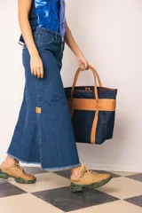 Falda larga de jean azul oscuro, corte amplio y recto, con abertura frontal y terminación desflecada en el ruedo. Presenta un pequeño parche de cuero marrón en la abertura lateral.