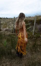 Pollera midi de cuero con estampado marmolado en tonos marrones y mostaza, de corte asimétrico con detalles de largos flecos colgantes en el borde inferior.