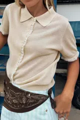 Chaqueta de punto celeste de manga corta con cuello polo, cierre frontal con botones y detalles de puntilla en color beige en la botonera y los puños.