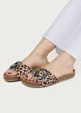 Sandalia plana con plantilla ergonómica y suela de corcho. Capellada de cuero con estampado animal print tipo leopardo y tira ancha ajustable con hebilla grande de resina translúcida en tono azulado.