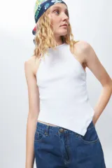 Top de algodón blanco sin mangas con cuello halter y bajo asimétrico en punta diagonal. Presenta un tejido de punto acanalado y un diseño inspirado en la estética de los años 2000.