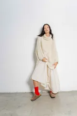 Sweater tipo poncho color crudo, tejido en punto grueso con cuello alto y mangas largas amplias.