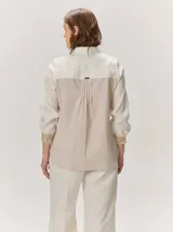 Camisa de lino color blanco con detalles combinados en tonos beige, cuello camisero, cierre frontal con botones oscuros y mangas largas con puños en contraste.