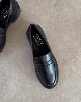 Mocasines negros de estilo clásico con textura de cuero grabado tipo cocodrilo. Presentan una banda frontal característica y suela plana con borde definido.