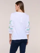 Blusa blanca de silueta semi entallada, confeccionada en tejido texturado. Cuenta con escote en V con abertura y vivo bordado multicolor, mangas 3/4 abullonadas con bordados, calados y puños elásticos.