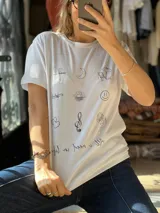 Remera blanca de manga corta con estampado frontal de múltiples ilustraciones minimalistas en línea negra y frase en la parte inferior.