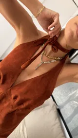 Vestido corto de cuero sintético color marrón, con diseño halter y escote profundo. Presenta un ajuste en el cuello, espalda descubierta y un volado ancho en el ruedo que aporta movimiento.