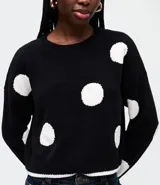 Suéter de punto con estampado de lunares blancos sobre fondo negro, cuello redondo, sisa desplazada y corte ligeramente corto.