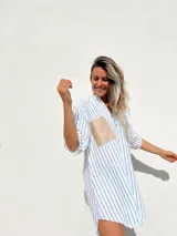 Camisola de corte oversize con estampado de rayas verticales azules sobre fondo blanco. Presenta cuello camisero, cierre frontal con botones y dos bolsillos frontales en contraste de color beige con acabado tipo gamuza.